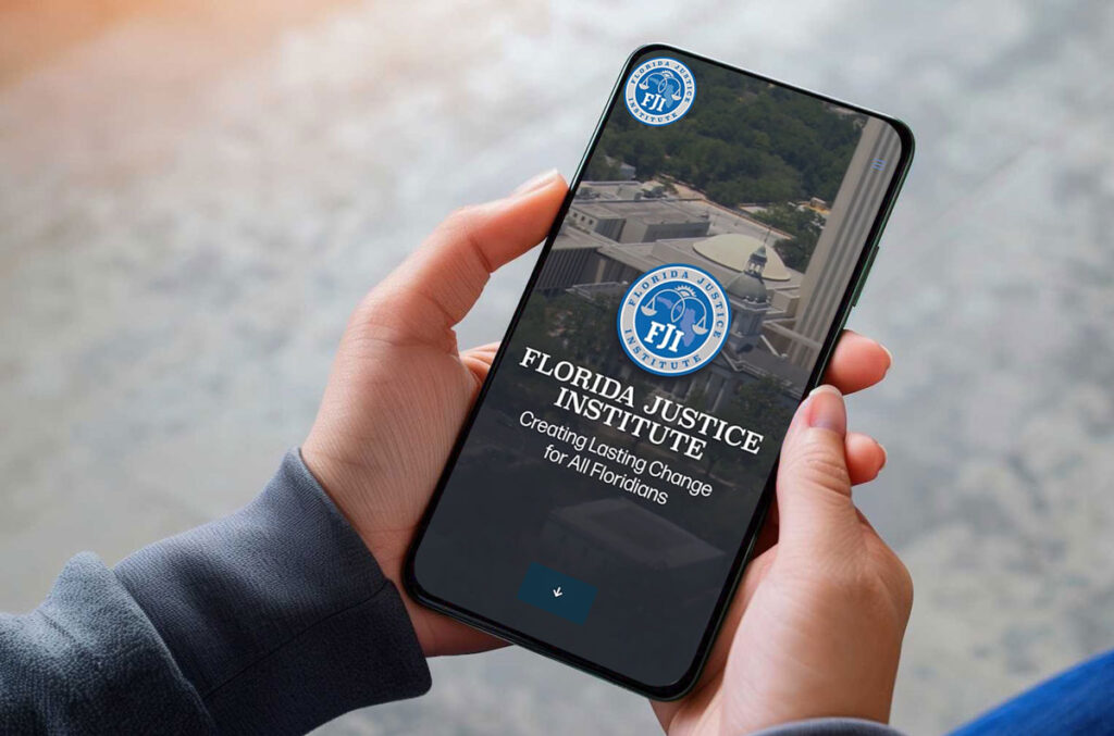 A picture of hands holding a cellphone with the home screen of FJI's website on the front